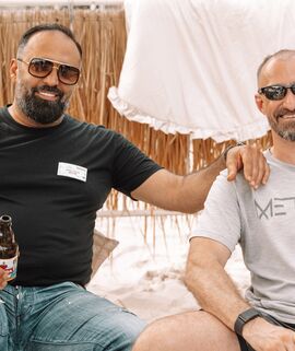 Sommerfest im blue:beach Witten. Zwei Männer mit Sonnenbrille sitzen mit Bier und Wasser im Sand.