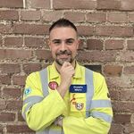 Ein freundlich schauender Mann in einer gelben Sicherheitsjacke mit dem Aufnäher "Donato Muro" vor einer Backsteinwand.