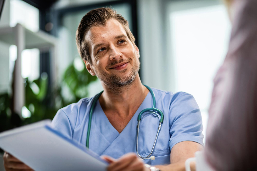 Glücklicher Betriebsarzt, der medizinische Unterlagen hält, während er während eines Arzttermins mit dem Patienten kommuniziert