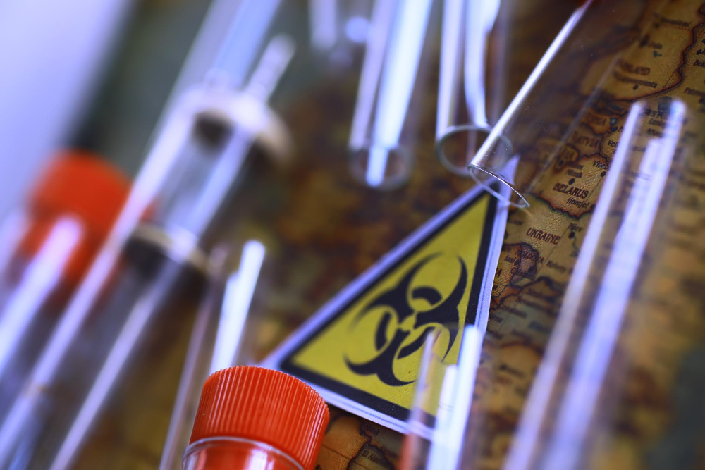 Ein Sticker mit dem Gefahrstoff-Symbol und mehrere Reagenzgläser in Nahaufname auf einer Landkarte.