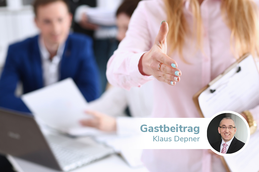 Eine Frau in rosa Bluse streckt die Hand aus. Sie hält ein Klemmbrett mit Zetteln unter dem anderen Arm. Im Hintergrund sitzen zwei Männer vor einem Laptop am Schreibtisch.