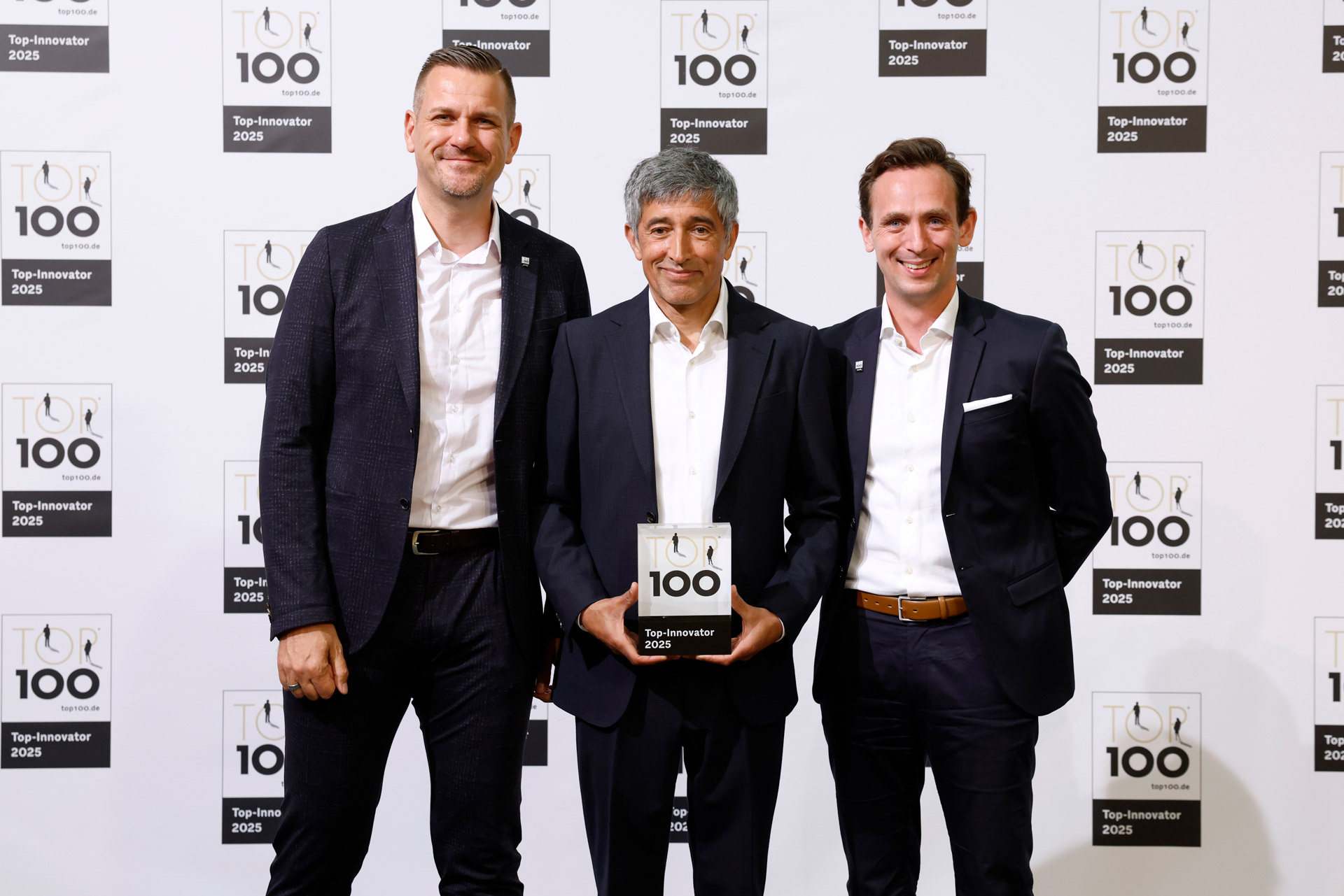 Foto von drei Männern in Anzug mit dem Siegel der TOP 100 Preisverleihung